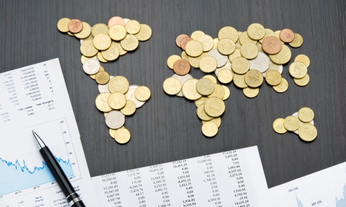 World map made out of coins next to charts and a pen