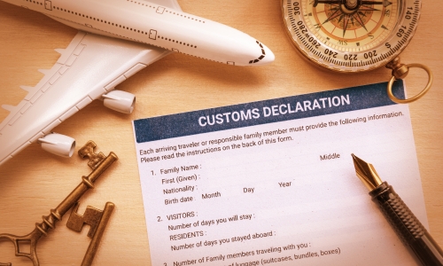 a customs declaration form with a pen, a compass, a modela airplane and two keys