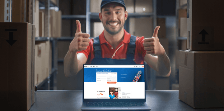 Shipa Freight workersurrounded by boxes looking at the camera with his thumbs up while showingshipa freigth's website on a computer