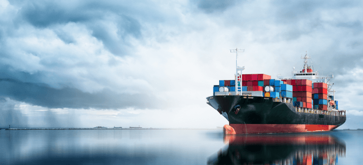 Cargo vessel loaded with shipping containers on a calm sea with cloudy sky above, en route to the United Arab Emirates
